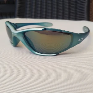 Vtg Oakley solglasögon  - Ett par turkos/blå-grönmetallic solglasögon från Oakley. Glasen är utbytbara. Spegelglasen har några små nagg som inte märks när man bär dem (därav priset). Sjukt grymma solglasögon 