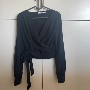 Blus - Snygg svart blus från NAKD! Omlott, knyte i midjan och dragkedja! 