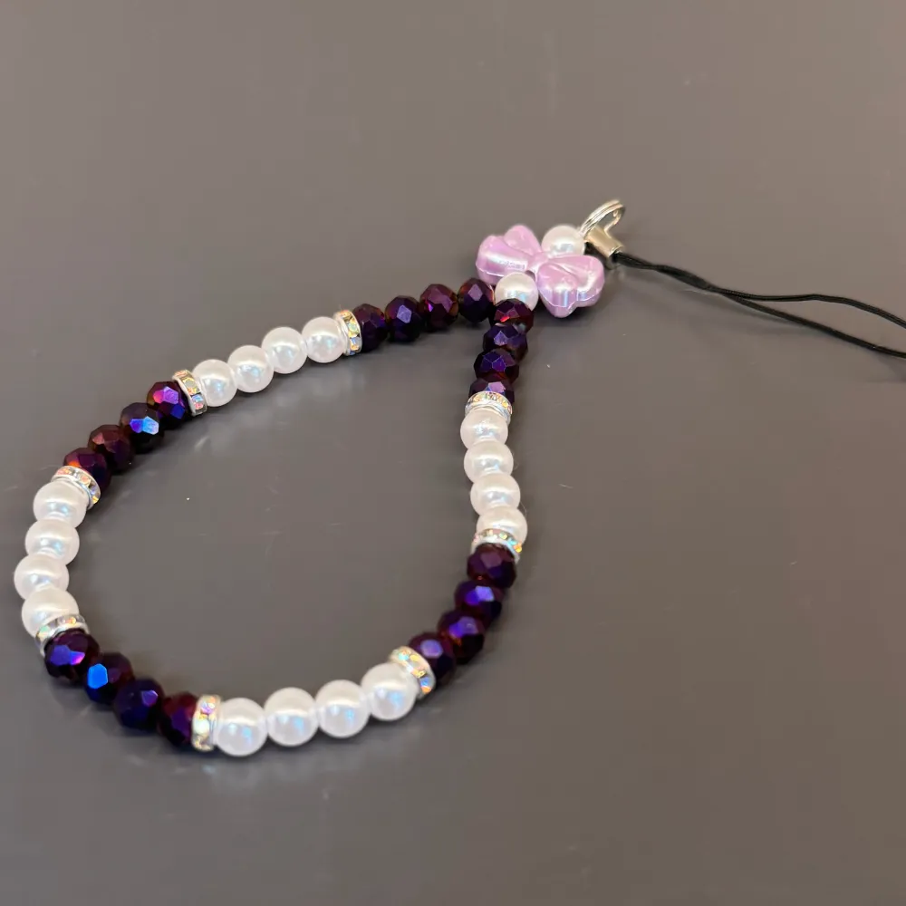 Egentillverkat mobilsmycke med lila o vita pärlor, blingiga mellanplattor och en söt lila. Är totalt 17 cm lång och med en omkrets på ca 18 cm.💜. Accessoarer.