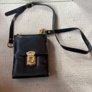 Retro handväska - Vintage väska i svart fake läder med gulddetaljer. Justerbar axelrem, tre olika lägen för stängning (om man har mycket saker packat). Och en innerficka med dragkedja. 