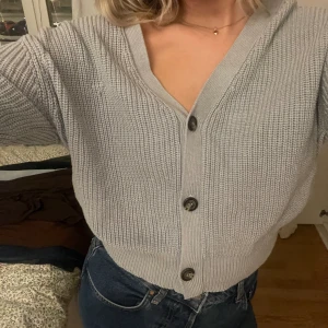 Grå stickad tröja  - Jättefin stickad kofta perfekt till sommarkvällen! Köpt för ett par år sedan men inte använt mycket. Någon tråd som är lös framtill men inte något som stör!