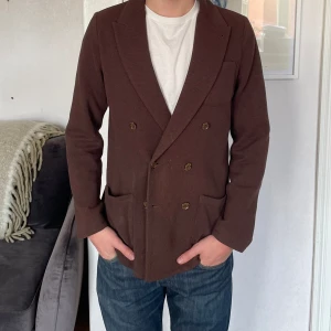 John Henric dubbelknäppt kavaj  - Super fin dubbelknäppt stickad kavaj från John Henric i en härlig brun färg.   Kavajen är i storlek S och personen på bilden är 179cm lång.   Kavajen är i fint använt skick, men skulle eventuellt må bra av kem då den har lite mindre fläckar. 