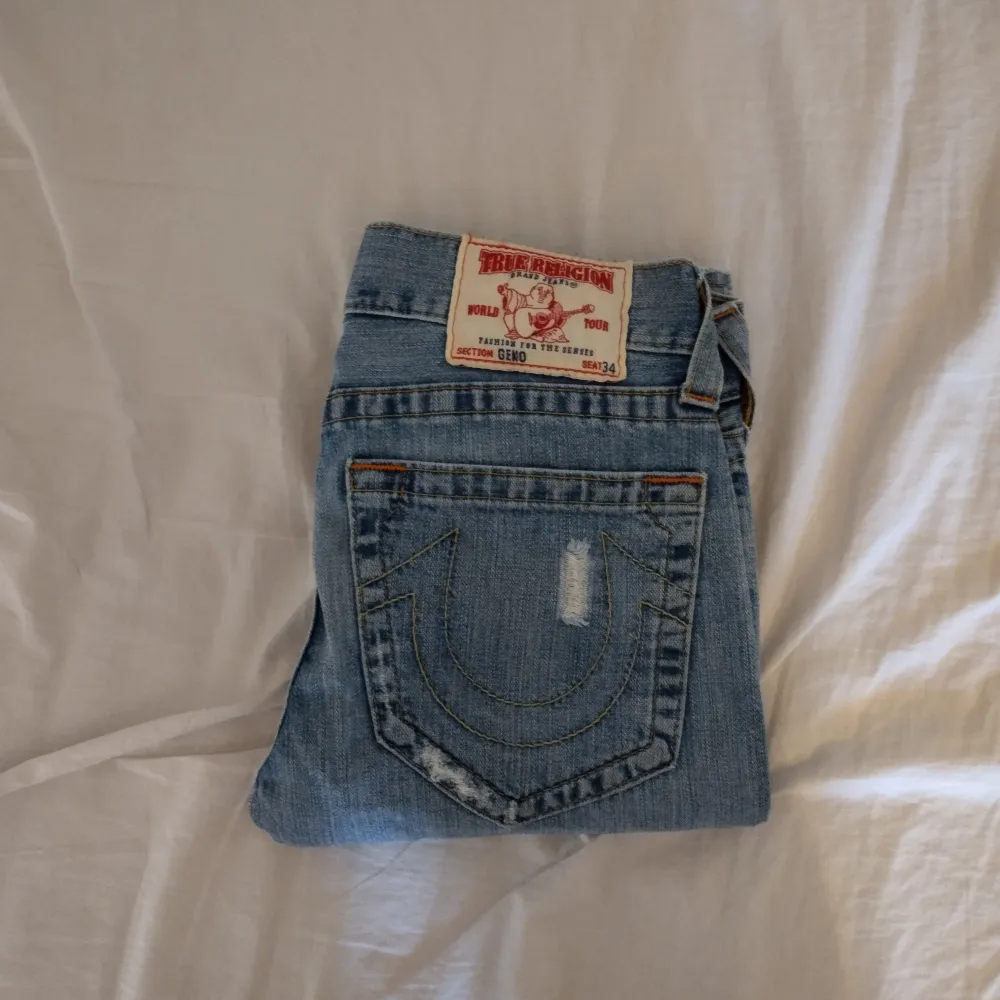 Ett par ljusblåa jeans från True Religion med hål, storlek 28 Midjemått: 39 cm Ytterbenslängd: 109.5 cm Innerbenslängd: 84 cm. Jeans & Byxor.