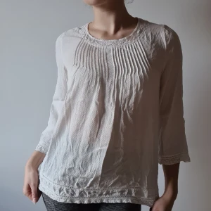 Vit blus med spetskrage - Fin vit blus med veckad utsmyckning över bröstet, med spetskrage & trekvartsärm från Long Island Hampton Republic. Hyskor i nacken.