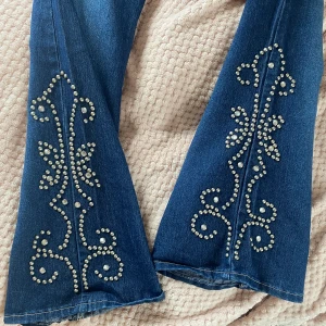 Bootcut jeans med coola detaljer - Lågmidjade bootcut jeans med coola detaljer på benen (en ”pärla” borta på höger ben)! 39 cm bredd, 102 cm full längd,  79 cm innerbenslängd. Säljer då de är för stora (jag är 166 cm). Skriv gärna i DM vid frågor 💗