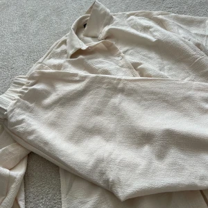 Beige set - Beige somrigt set med matchade skjorta och byxor.   Vita knappar längs med skjortan.   Endast använd 2-3 gånger, säljer pga att den blivit för liten.   Storlek XS med sitter mer som S då den är oversized.   Nypris: 329kr
