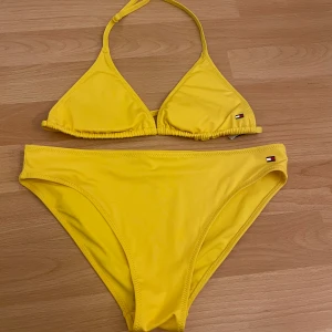 Bikini  - Säljer en gul Tommy hilfiger bikini. På rumpan så finns det en silvrig text för det står Tommy. Den är i storlek 14-16 år.