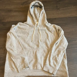 Grå hoddie  - En grå hoddie från H&M i storlek M. Bra skick men lite sliten och en fläck vid snöret som man ser på andra bilden. Men annars är snörena snygga och liknar skosnören. 