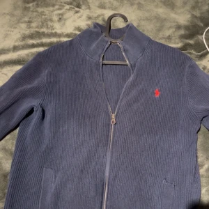 Polo Ralph Lauren Helzip - Helzip Polo Ralph Lauren i mörkblå färg.  Skick: 6/10  Tröjan har använt ett par gånger och lossnat lite vid ena zippen längst ned (se bilden)  Samt att lappen i nacken är lös på ena sidan och att ena fickans öppning är lite lös. (Kom dm för bilder)