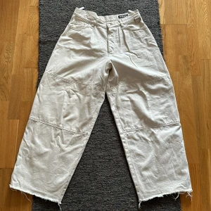 Beige byxor från Hope - Ett par vita jeans från Hope med en lös passform. Byxorna har en hög midja och vida ben. De har en rå kant vid bensluten och är av bomull. Byxorna har fickor både fram och bak samt en dekorativ metallring vid ena fickan. Köpta av mig från hope. Hör gärna av er om ni har några frågor eller liknande!
