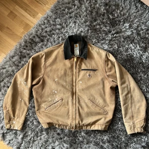 GENUIN VINTAGE Carhartt Detroit Work Jacket - Svinfet Carhartt jacka importerad från USA. Köpt på ettresex i Stockholm. Genuin wear på allra bästa sätt. Se bilder för detaljer. Boxy fit, storlek 2XL men passar även XL. Perfekt höstjacka.  Mått:  65 cm på bredden 79 cm på längden 67 cm ärmlängd