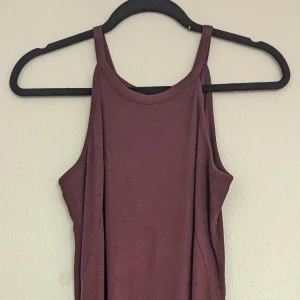 Vinröd klänning från Gina Tricot - En ärmlös vinröd klänning från Gina Tricot. Klänningen har en enkel design med rund hals och är tillverkad i ett ribbat material. slutar nedanför knäna