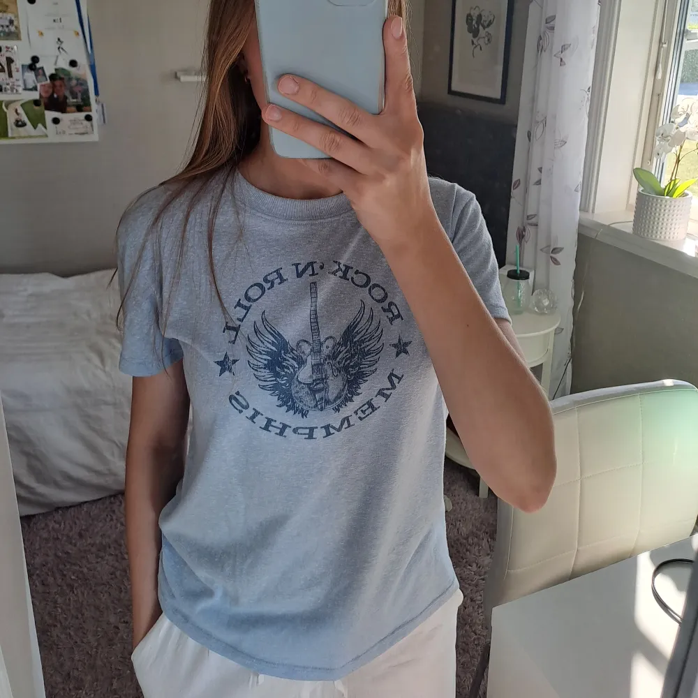 En ljusblå t-shirt med ett tryck av en gitarr med vingar och text. T-shirten har korta ärmar, en rund halsringning och väldigt skönt material.✨️. T-shirts.