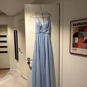 Balklänning ljusblå - Ljusblå balklänning i fodrad chiffong använd vid endast ett tillfälle. Klänningen är kemtvättad och har inga defekter. Personen på bilderna är 167cm. Nypris 2500 kr och köpt på dressroom linne Göteborg. Storlek 34/36 och medföljer en klädgaderob. 