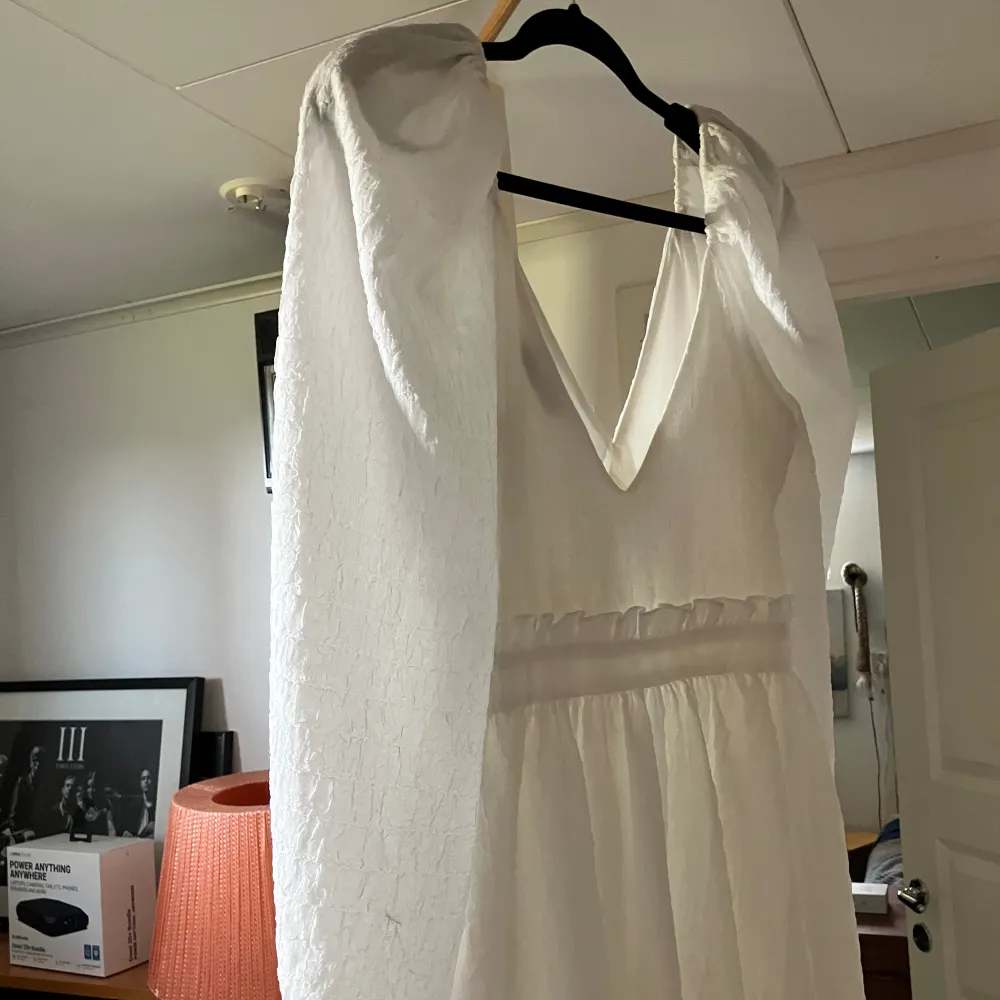 En kort vit klänning med ballongärmar. V ringad och mini volang detalj under bysten. Lite vid och väldigt följsam kjoldel på klänningen. Använd två gånger, fint skick. Ordinarie pris . Klänningar.