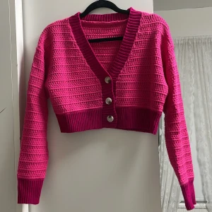 Stickad kofta - oanvänd - Stickad tröja, kort i längden. Färgen är skrikrosa. Köpt för 150kr säljer för 60kr.