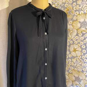 Margit Brandt Copenhagen. Skjorta, mörkblå med kontrastsömmar i gråblått. Längd fram 60 cm, bak 90 cm. Knyt i halsen. Märkt med small, passar stl 38. 