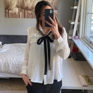 Vit blus - En jättefin vit blus med knappar där framme och ett svart snöre man kan knyta. 