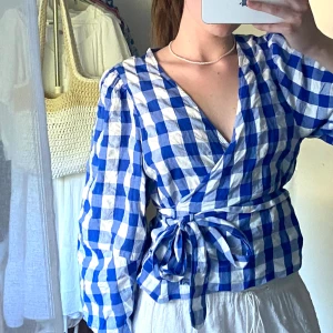 Omlottblus från Lindex, strl. S - Säljer denna fina blårutiga omlottblus från Lindex som tyvärr inte kommer till användning. 100 % Bomull. Fint skick utan anmärkningar. 