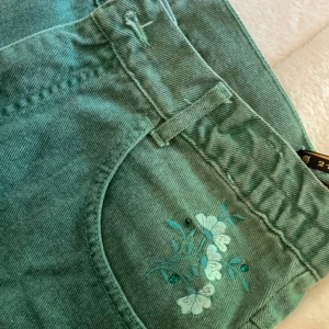 Gröna Jeans - Gröna Jeans med blommig detalj. (OBS: Söndrig kamera därav de suddiga bilderna)