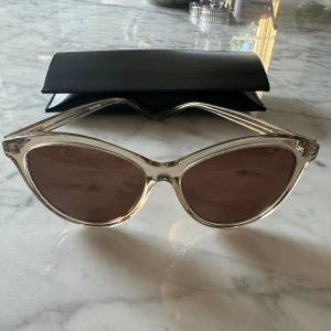 Saint Laurent Solglasögon - Supersnygga Cat-eye solglasögon i genomskinlig greige-färg. Har använts ett fåtalgånger och är därför i mycket bra skick. Dock finns ett litet jack på insidan men det är inget som syns när de är på.