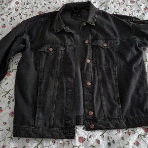 Oversize Jeansjacka - En oversize svart jeansjacka från Monki. Storlek: M. Har fyra fickor. Lite uttvättad stil på jeanstyget. Kopparfärgade knappar. 