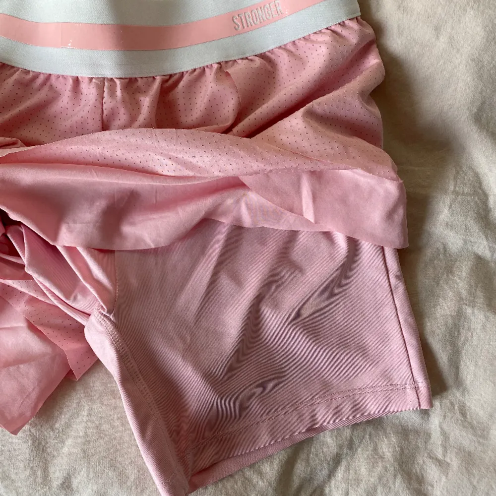 Träningsshorts från Stronger. Rosa med tightare innershorts och volang utanpå. Säljer då de var något stora på mig. . Shorts.