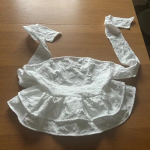 Vit bandeau topp - Säljer denna vita bandeau topp med Blom ditaljer som man kan knyta i ryggen. Storlek M men passar S! Aldrig använd då den inte passade