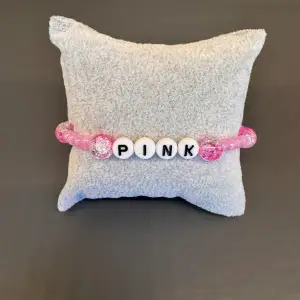 Egentillverkat pärlarmband med rosa pärlor och med texten ”PINK” med svart-vita pärlor. Är gjort med gummitråd och är ca 17 cm långt.