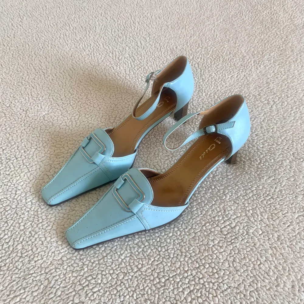 Otroligt vackra låga klackskor / kitten heels i en fin ljusblå färg med spänne. Aldrig använda, men finns några små prickar och skador på ena skon (se bild), det syns knappt och stör inte användningen. Säljer även storlek 38 i annan annons.. Skor.