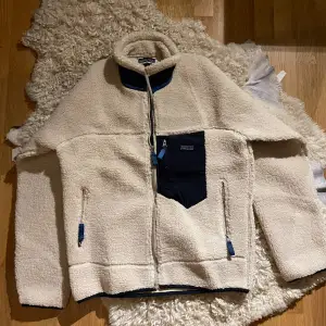 Introducing a stylish beige Patagonia fleece jacket in excellent condition (9/10). This cozy and versatile outerwear piece not only provides warmth but also complements your wardrobe with its neutral hue. 