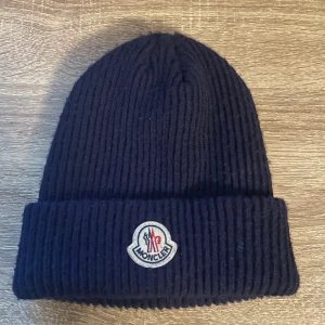 Moncler mössa - Navy blue moncler mössa. Helt oanvänd så väldigt fint skick. Vill bli av med den så fort som möjligt för ska iväg så priset är inte skrivit i sten och kan sänkas vid snabb affär!