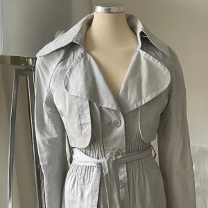 Trenchcoat ny med prislappen kvar  - Trenchcoat från Vero Moda Designes Choice  Köpt i Köpenhamn  Färgen är grå/silver med lite glans 