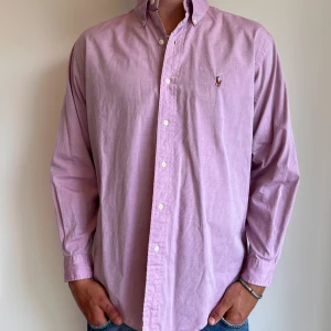 Ralph Lauren skjorta  - Rosa Ralph Lauren skjorta i storlek 15,5 vilket motsvara ca L. Modellen är något kort i ärmarna. Skjortan är i fint skick utan några skavanker. Modellen är 186 cm lång. Orginalpris ca 1500 kr och nu endast 499. 
