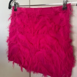 Cerise rosa set  - Ett cerise rosa set med en kjol och en halterneck topp med ”fransar”. Öppen i ryggen med två snören som knyts i ryggen, samt knyte i nacken.  Från Na-Kd, använd fåtal gånger, fint skick! 