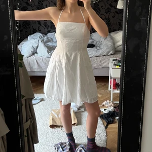 Vit kort klänning - En helt ny/oanvänd vit sommarklänning från NAKD. Kort längd med öppen rygg och snören som är justerbara i ryggen. Köptes i år för 400 kr men för liten för mig 