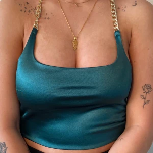 Mörkgrön silkeströja med guldkedja - Mörkgrön silkesmagtröja med en guldkedja som knyts runt halsen. Storlek S. Aldrig använd, legat och skräpat i garderoben då jag bytt klädstil. Nyskick.