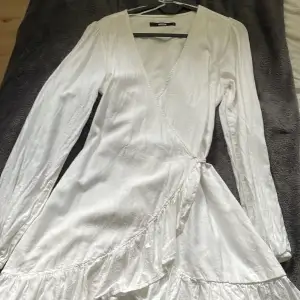 En vit långärmad klänning från BikBok, använd bara 1 gång. Storlek S med knyt vid sidan om.  Perfekt till sena sommarkvällar om man vill ha en vit klänning och inte biten av mygg på ärmarna.