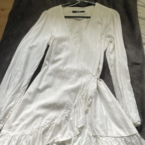 Fin vit volang långärmad klänning - En vit långärmad klänning från BikBok, använd bara 1 gång. Storlek S med knyt vid sidan om.  Perfekt till sena sommarkvällar om man vill ha en vit klänning och inte biten av mygg på ärmarna.