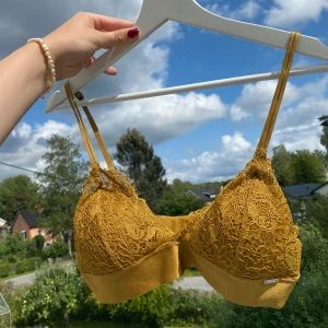 Gul spets-bh från Ella M - En elegant gul/guldig spets-bh från Ella M med justerbara axelband och hakknäppning bak. Bh:n har en vacker spetsdesign och är tillverkad i ett mjukt och bekvämt material.🥳🌟Knappt använd!