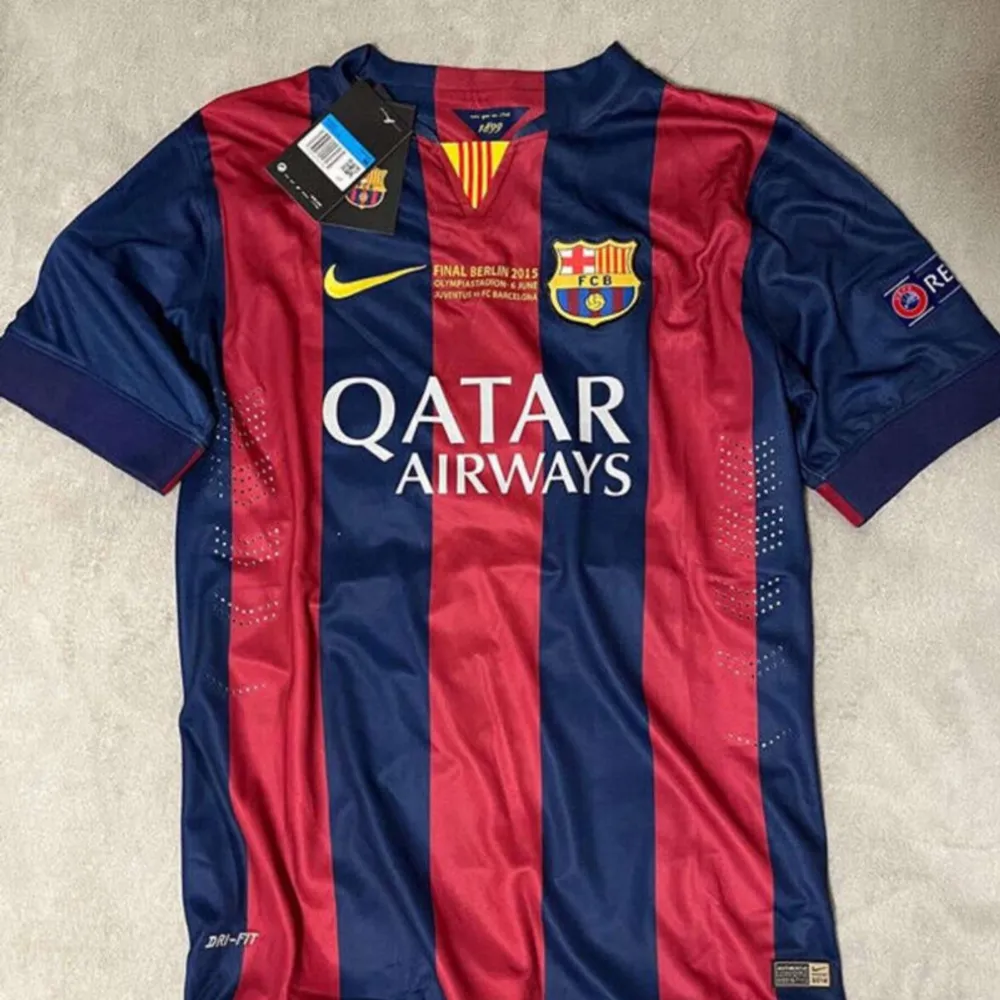 En blå och röd randig fotbollströja från FC Barcelona med Qatar Airways som sponsor på framsidan. Tröjan har korta ärmar och är i nyskick. På baksidan finns namnet 'Messi' och nummer 10 i gult. Tröjan har även Champions League-märke på ärmen och UNICEF-logga på nedre delen av ryggen.. Sportswear.