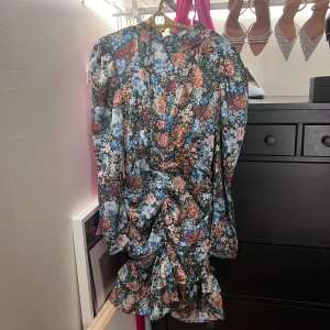 Blommig klänning i siden liknande tyg - Sitter jättefint på. Draperad. Använt skick. Dragkedja i sidan. Puffärm. 
