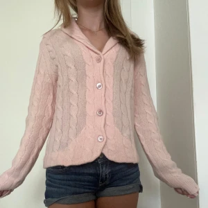 Rosa stickad kofta - En mjuk och bekväm rosa stickad kofta med kabelstickat mönster. Koftan har långa ärmar och knappar framtill. Aldrig använd! köparen står för frakt. Storlek M men jag har vanligtvis xs.