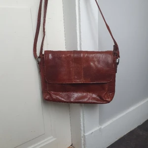 Axelbandsväska - Skinnväska.  Mått ca 30x20 cm.  1 fack bak på väskan,  i fram och 2 inuti.