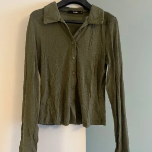 Grön, glittrig meshtopp - Grön meshtopp med glittriga inslag och knappar fram, samt krage. Köpt på BikBok i storlek M. I gott skick, sparsamt använd. 