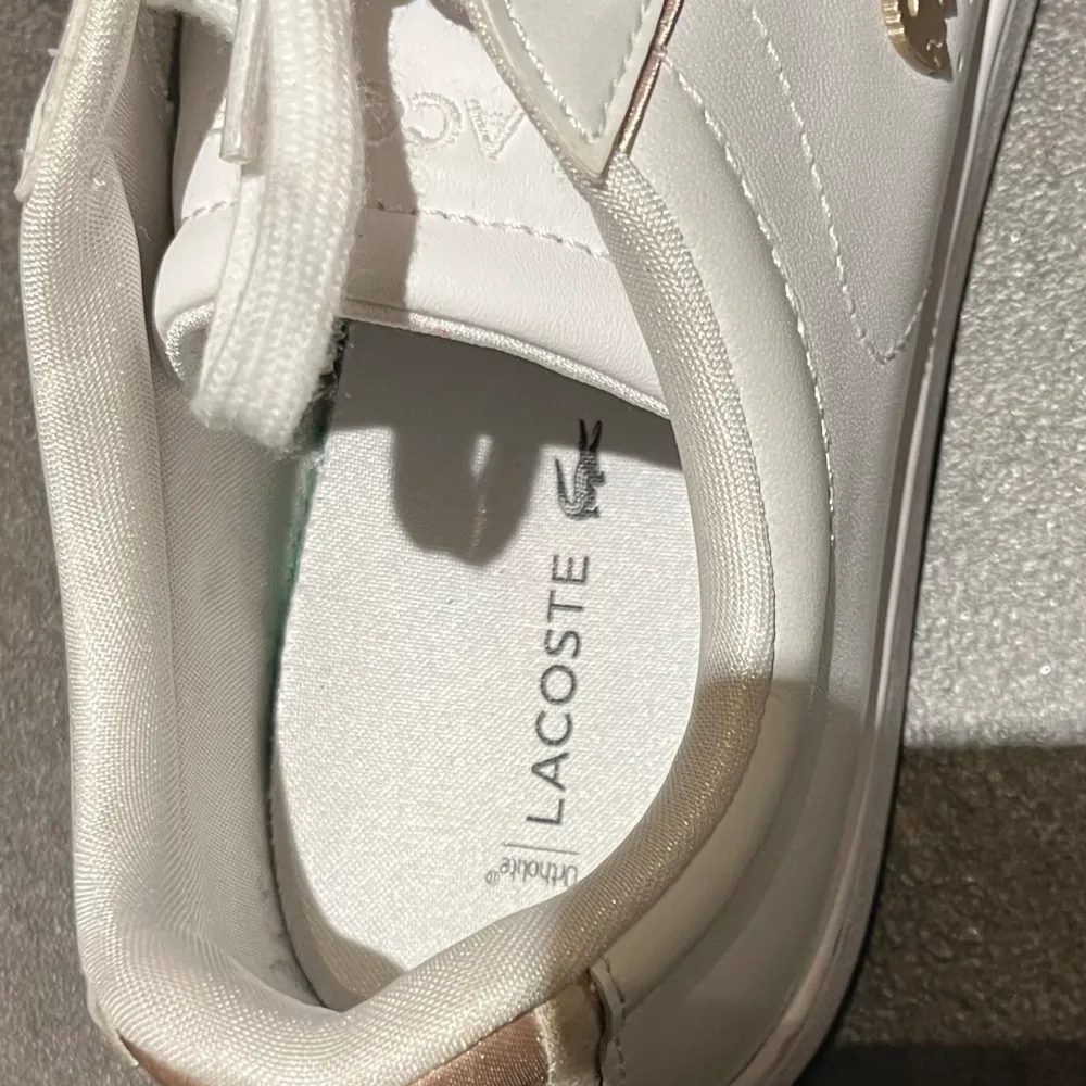 Vita Lacoste sneakers med guldiga detaljer. Använda 2 gånger, nästan nyskick, lite smutsig närmre sulan. Säljer då de är för små för mig.. Skor.