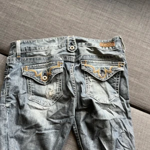 Lågmidjade jeans med vintage detaljer - Lågmidjade Jeans med snygga vintage detaljer. Märket ”Guess”  Tyvärr har en av knapparna på ena bakfickan låstnat därav det låga priset (se bild)!  Utländska storlekar men den står som 30 (se bild) skulle nog passa typ 36. Köpare står för frakten💕