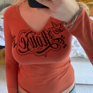 Orange långärmad topp - Orange långärmad topp med tryck på. Trycket läser ”House”. Magtröja. 