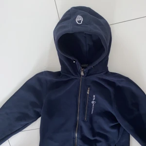 Sail racing zip up  - Sail racing zip up hoodie. Storlek 170. Nyskick och säljer för att behöver pengarna. Köpte för 1500kr på Sail Racing sidan. Säljer nu för 800kr. Använts fåtal gånger men är i nyskick. Säljes snabbt