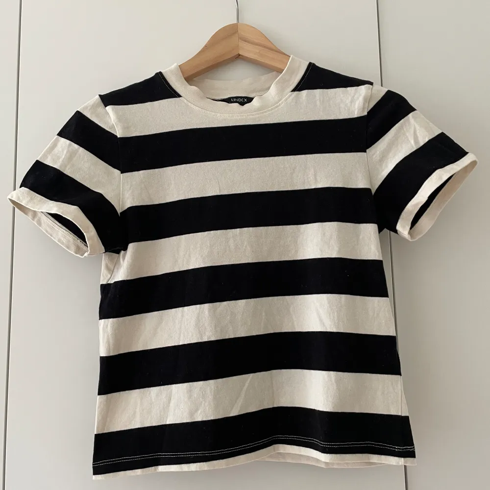 En beige svart randig t-shirt ifrån Lindex. Tröjan är i en väldigt snygg modell och lite kortare än en ”vanlig” t-shirt. Endast använd 2 gånger, så i bra skick🥰😍💗💘. T-shirts.
